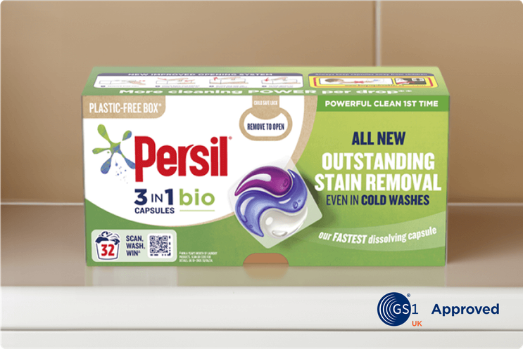 Close-up view of a box of Persil 3-in-1 Bio Capsules on a white counter with beige tiles in the background. The packaging highlights features like “Outstanding Stain Removal,” “Even in Cold Washes,” and “Plastic-Free Box.”