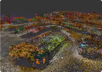  colorful 3D point cloud rendering of an urban area, showing clustered points forming roads, vehicles, and greenery from a top-down perspective.