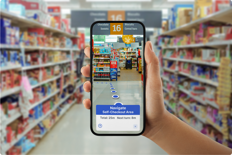A hand holding a smartphone in a brightly lit grocery store aisle, showing an augmented reality path of blue markers on the floor directing the user to “Colman’s Recipe Mix 24g” in aisle 16, between sections for sweets and cereal bars.